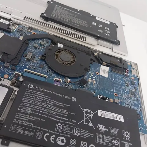 Notebook aberto na bancada com a bateria nova instalada ao lado da antiga