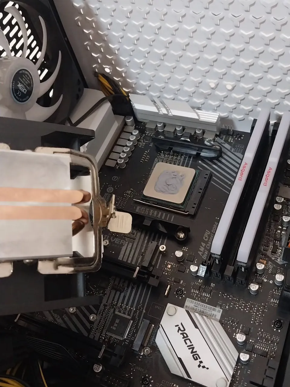 Placa-mãe na bancada da D&M com pasta térmica aplicada no processador e cooler sendo instalado