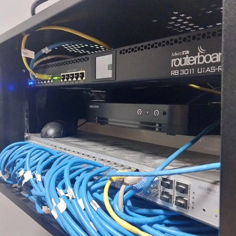 Rack de rede com RouterBoard MikroTik RB3011 e cabos azuis organizados e identificados