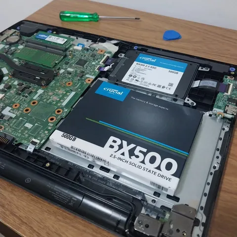 SSD Crucial BX500 de 500 GB sendo instalado em um notebook aberto sobre a bancada